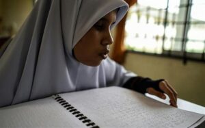 دانش‌آموز دحتر که مقنعه سفید به سر دارد و در حال خواندن بریل است.