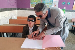 آقای آموزگار در حال کار با دانش‌آموز پسر نابینا به صورت انفرادی در کلاس