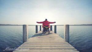 فردی با ویلچیر روی پل رودخانه است و دستهایش را به دو طرف باز کرده است