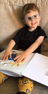 کودکی که عینک به چشم دارد، کتاب تصویر برجسته را روی پایش گذاشته و لمس می‌کند