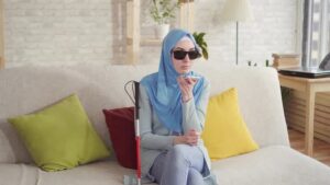 خانم نابینا با عینک دودی و عصا روی مبل نشسته