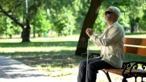 آقای سالمند نابینا روی نیمکت پارک نشسته