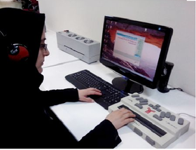 خانم کارمند نابینا در حال کار با کامپیوتر و با استفاده از برجسته نگار است و هدفون روی سر دارد