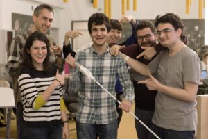 مرد جوان نابینا، عصای سفید در دست دارد و دوستانش در اطراف او هستند